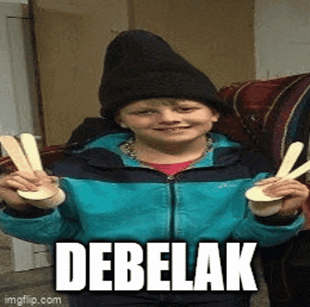 a young boy wearing a black hat and a blue jacket is holding two wooden spoons and the word debelak is above him
