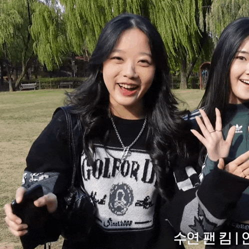 a girl wearing a golford sweater smiles while standing next to another girl
