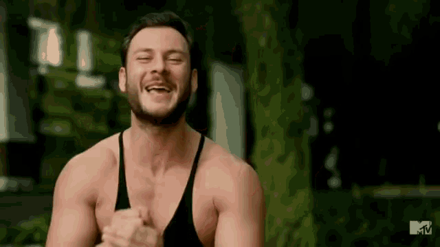 a shirtless man with a beard is laughing with his eyes closed while wearing a black tank top .