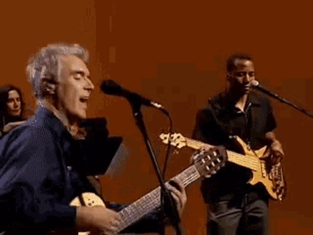 a man singing into a microphone while another man plays a guitar on stage
