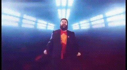 a man with a beard in a suit and red shirt is standing in front of a large screen .