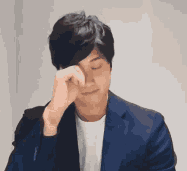 a man in a blue suit is covering his face with his hand .