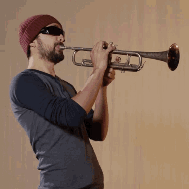 a man wearing sunglasses and a red beanie is playing a trumpet