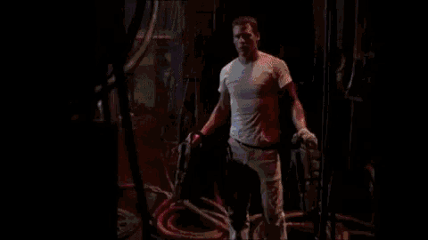 a man in a pink shirt is standing in a dark room with a purple light behind him .