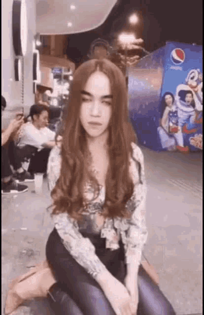 a woman with long red hair is kneeling down in front of a pepsi ad .