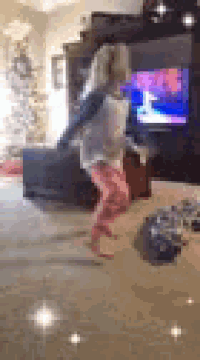 a little girl is jumping in the air in a living room in front of a television .