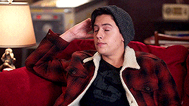 a man is sitting on a red couch wearing a plaid jacket and a hat .