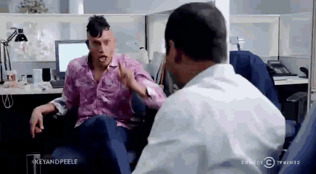 two men are having a conversation in an office cubicle .