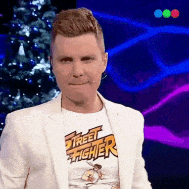 a man wearing a street fighter t-shirt stands in front of a christmas tree