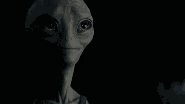 a close up of a gray alien with blue eyes in a dark room .
