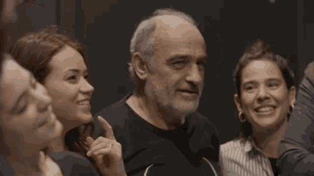 a man with a beard is surrounded by three women and one of them is smiling