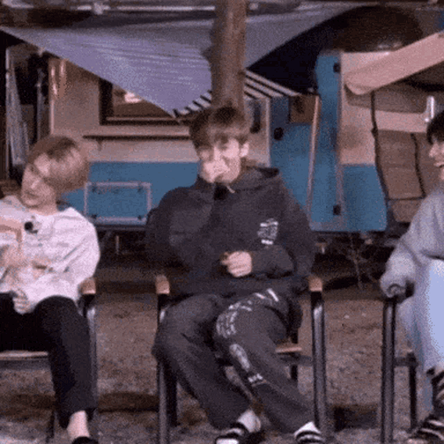 a group of people are sitting in chairs and one of them is covering his face with his hand .