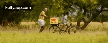 a man is pushing a bicycle with a box on the back through a grassy field .