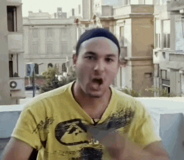 a man wearing a yellow t-shirt and a black hat is standing on a balcony .