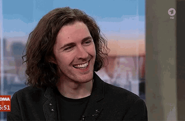 a man with long hair is smiling in front of a screen that says oma 5:51