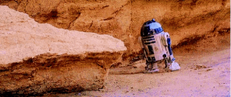 r2d2 from star wars is standing next to a large rock in the desert