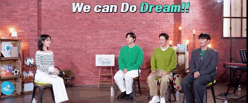 a group of people are sitting in chairs in front of a brick wall talking to each other .