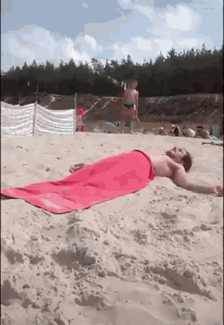 a man laying on a beach with a pink towel on his back