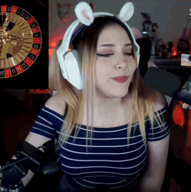 a woman wearing headphones with a rabbit ear headband stands in front of a roulette wheel