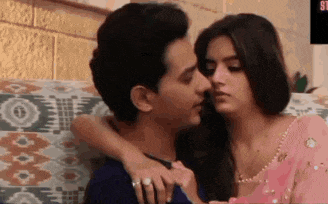 a man and a woman are kissing on a couch . the woman is wearing a pink saree .
