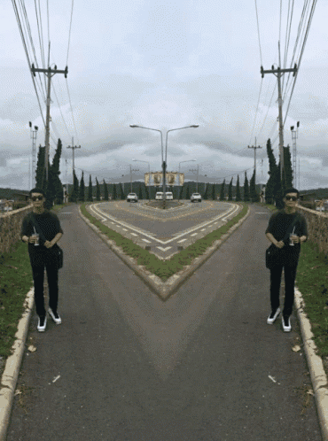 a man is standing in the middle of a road with a reflection of himself in the road
