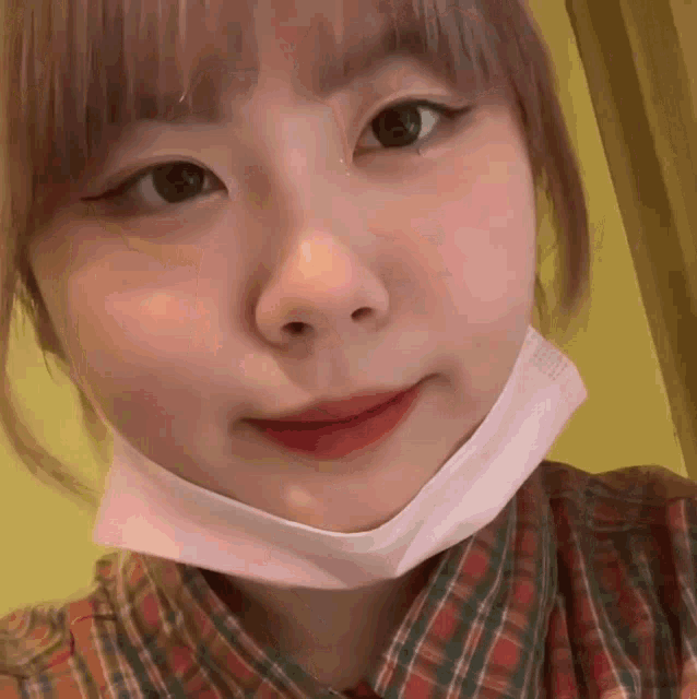 a girl wearing a pink mask and a plaid shirt smiles