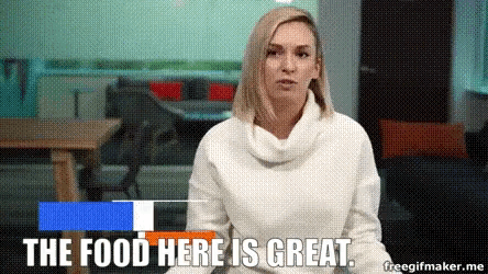 a woman in a white sweater is sitting in front of a sign that says the food here is great