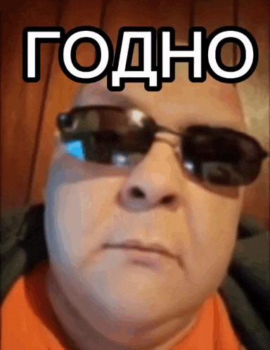 a man wearing sunglasses and an orange shirt has a foreign language written on his face