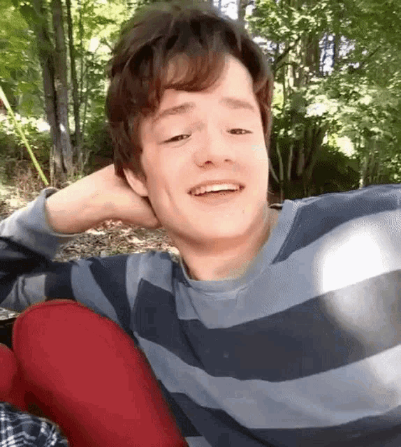 a young man in a striped shirt is smiling while sitting on a red chair .