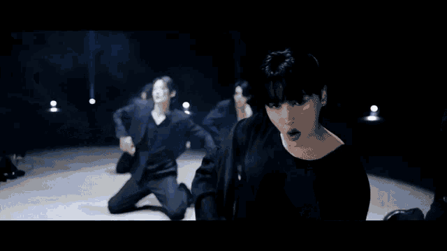 a man in a black shirt is standing in front of a group of dancers