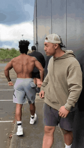 a man without a shirt is leaning against a wall while another man holds his hand .