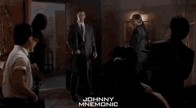 a man in a suit and tie is standing in a dark room with johnny mnemonic written on the bottom