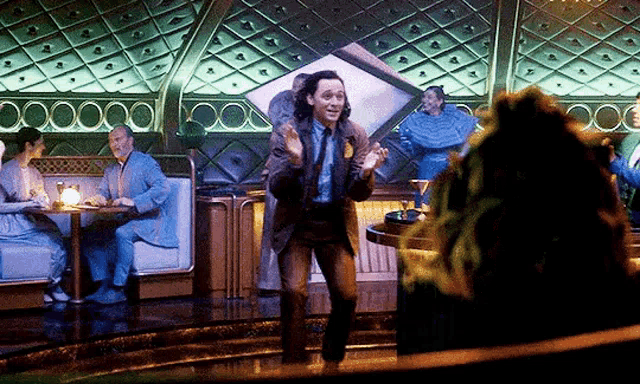 a man in a suit and tie is dancing in a room with people sitting at tables in the background .