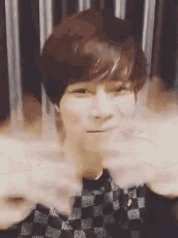 a young man with short hair is making a funny face with his hands in front of his face .