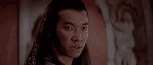 a man with long hair is standing in front of a wall .