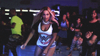 a woman in a wonder woman shirt is dancing in front of a crowd of people
