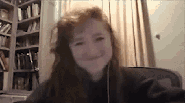 a woman is sitting at a desk in front of a bookshelf and smiling at the camera .