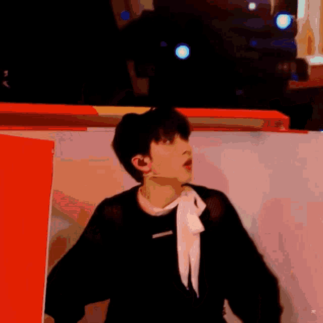 a young man wearing a black shirt and a white scarf is dancing on a stage .