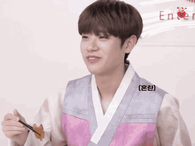 a young man wearing a pink and grey kimono is holding chopsticks