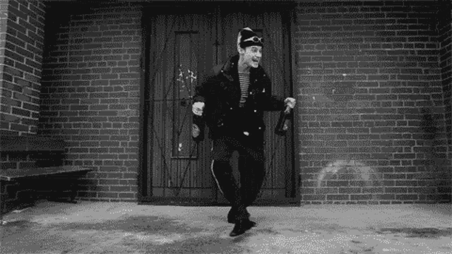 a man is dancing in front of a brick building while holding a bottle of beer .