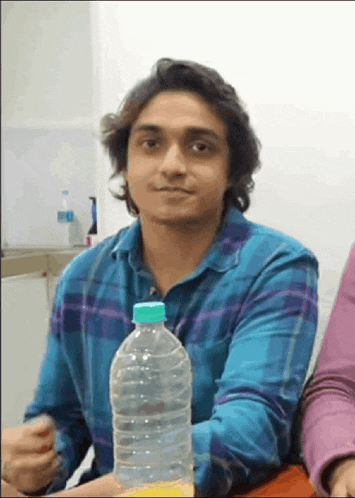 a young man in a blue plaid shirt holds a bottle of water