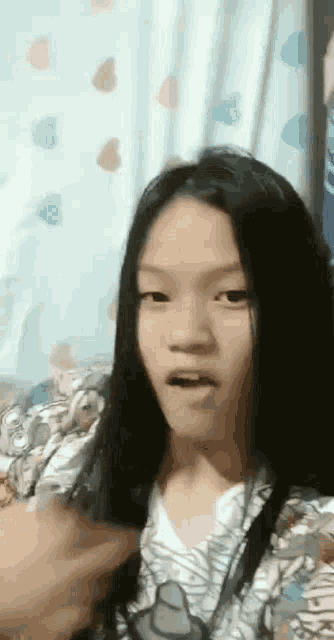 a young girl with long black hair is making a funny face while sitting on a bed .