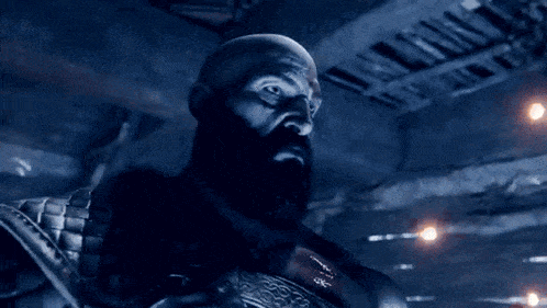 a bald man with a beard is standing in a dark room with lights on the ceiling
