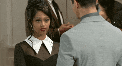a woman in a black dress with a white collar looks at a man in a suit
