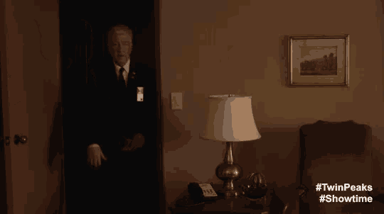 a man in a suit and tie is standing in a room with a lamp and says coffee time