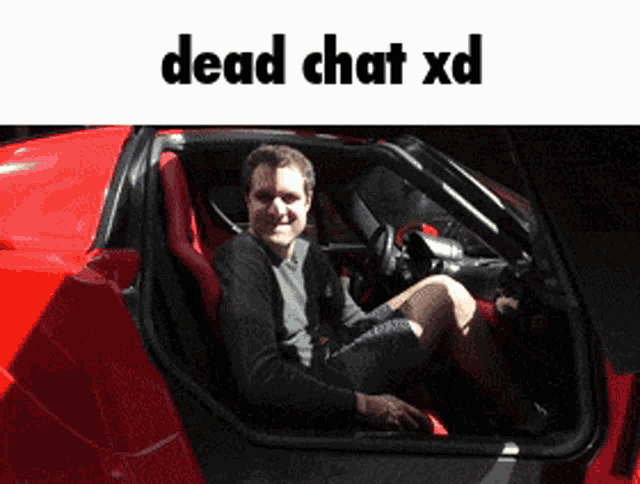 a man is sitting in the driver 's seat of a red sports car with the words dead chat xd below him