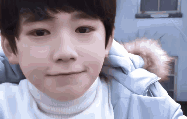 a young boy wearing a white turtleneck and a blue jacket with a fur hood