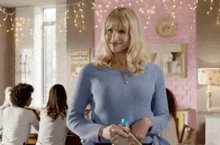 a woman in a blue sweater is standing in a room with a sign that says coffee on the wall .