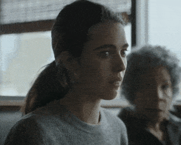 a woman wearing a grey sweater and earrings looks at the camera