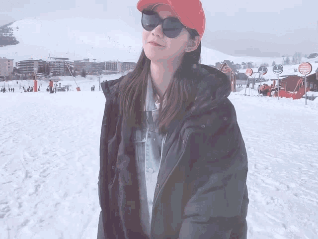 a woman in a red hat and sunglasses stands in the snow